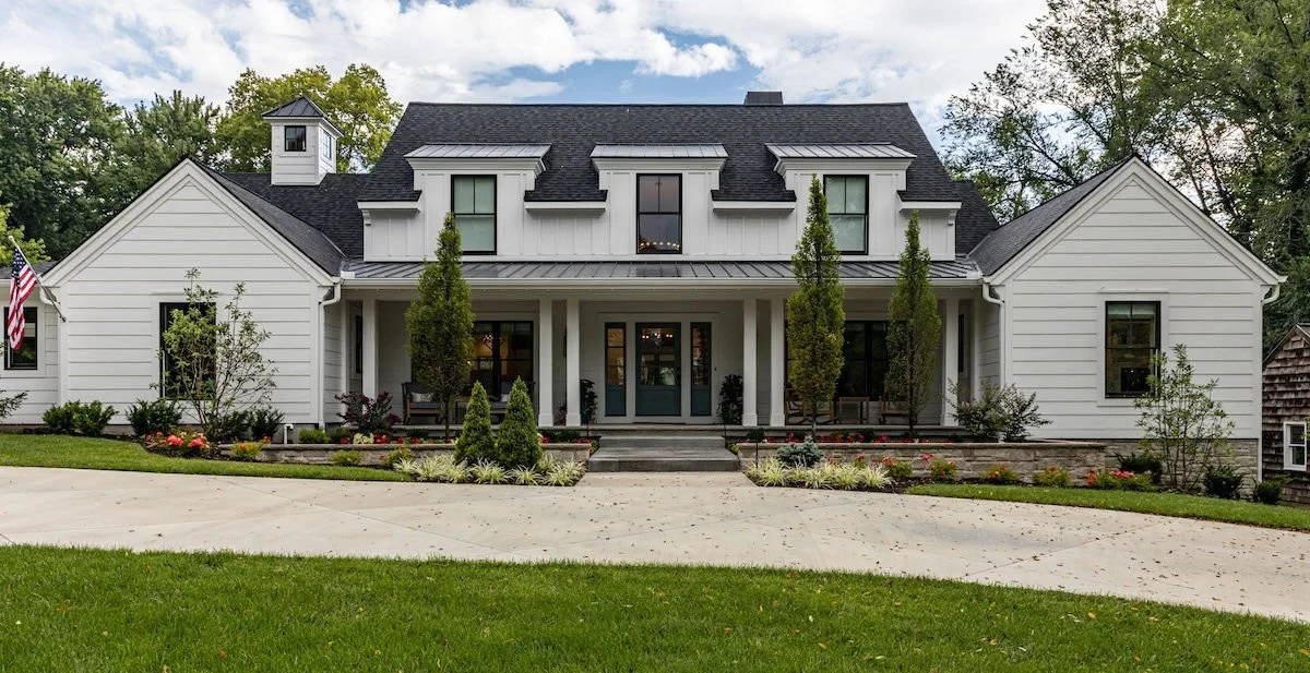 White home with a broad front lawn, curved driveway, and planted garden beds
