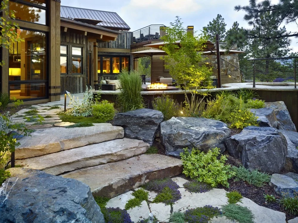 Natural stone steps and boulders woven through planting beds beside a residential patio and fire feature
